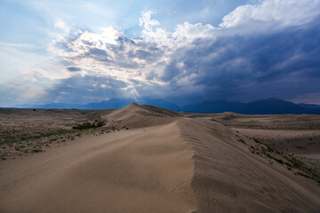 Vast desert dunes under a dramatic sky with sunbeams
