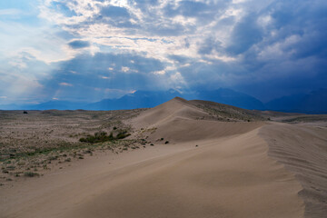 Vast desert dunes under a dramatic sky with sunbeams