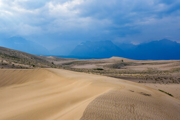 Expansive desert dunes under a dramatic sky with distant mountains