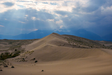 Fototapeta premium Dramatic desert dunes under sunbeams and cloudy sky