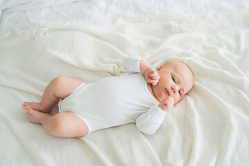 Happy baby. Cute little newborn girl with smiling face lying on bed in bedroom. Infant baby resting...