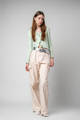 Woman in Green Cardigan and Beige Cargo Pants Poses Against a White Wall