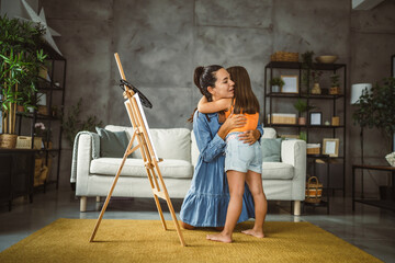 Mother teach mentor daughter to create art at home on easel with brush