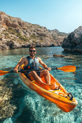 Portrait of a happy male in kayak boat exploring rocky valley in shallow sea