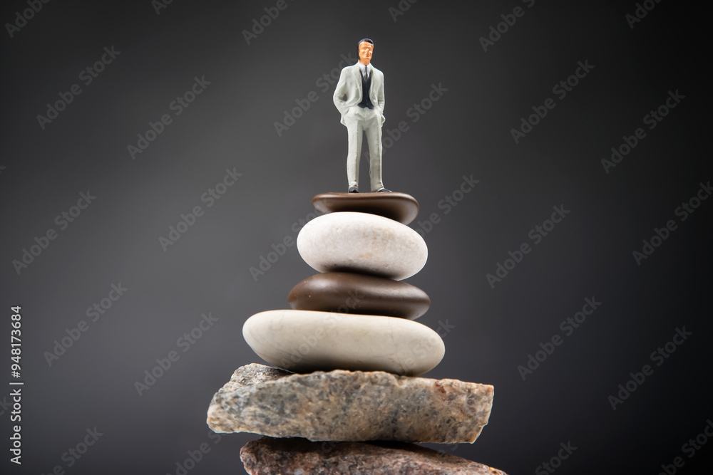 Wall mural miniature people. the figure of a man stands on top of the stones. concept of achievements in life and success in business.