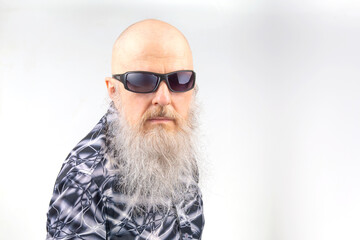 portrait of a successful bald man with a large gray beard wearing sunglasses on a light background.