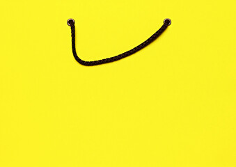 Close-up of yellow shopping bag with black handles, symbolizing the concept of shopping and retail. Banner, poster. Concept of shopping, Black Friday, Cyber Monday. Copy space for ad, text