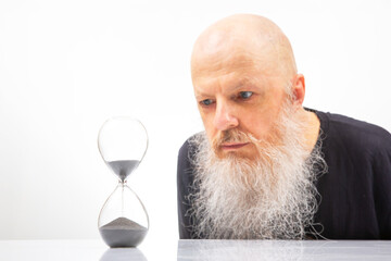 Intense focus on an hourglass by a bearded man, portraying the relentless flow of time. The...