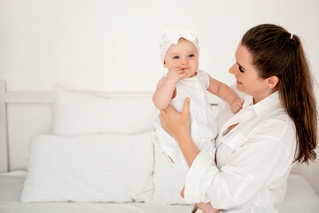 mom and baby hug and kiss at home on the bed in the bedroom, parental love and care, happy motherhood, mom with a baby in her arms, space for text