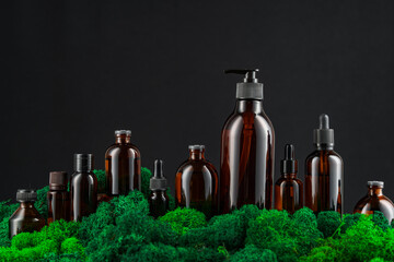Dark glass bottles arranged on green moss against a black background