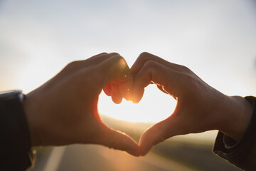 Hands in the shape of heart against the sunrise