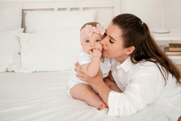 mom and baby hug and kiss at home on the bed in the bedroom, parental love and care, happy motherhood, mom with a baby in her arms, space for text