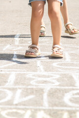 Closeup of little girl legs and hopscotch drawn on asphalt. Child playing hopscotch game on playground outdoors on a sunny day. Summer activities for children.