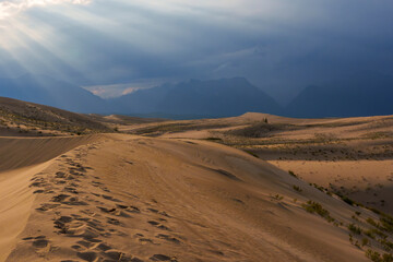 Dramatic desert dunes under sunbeams and cloudy sky