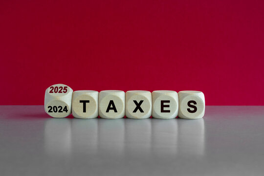 2025 taxes new year symbol. Turned a wooden cube and changes words Taxes 2024 to Taxes 2025. Beautiful grey table pink background. Business 2025 taxes new year concept.