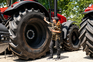 A woman with a digital tablet in her hand touches a large wheel of a construction or agricultural...