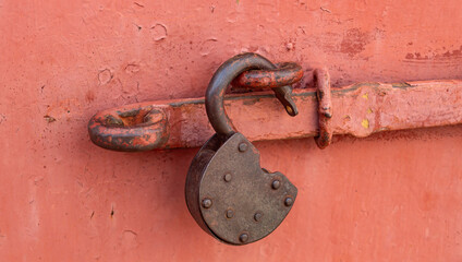 An old rusty iron padlock hangs on a red iron garage door