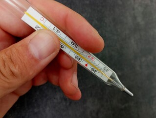A glass mercury thermometer for measuring body temperature in a human hand on a black textured background. Medical thermometer.