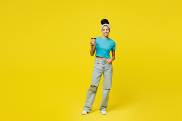 Fototapeta premium Full body young Latin woman she wears blue top t-shirt headband casual clothes hold takeaway delivery craft paper brown cup coffee to go isolated on plain yellow background studio. Lifestyle concept.