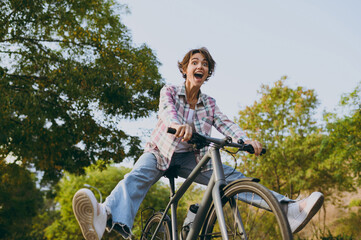 Side view young woman wear checkered shirt casual clothes look aside walk riding bicycle with...