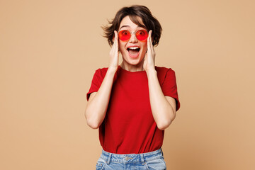 Young shocked surprised fun happy woman wear red t-shirt casual clothes sunglasses look camera put...