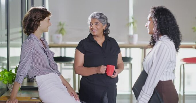 Indian young adult women intern old aged lady hold cup mug drink coffee talk gossip work place expert teen girl staff group team speak idea blab share enjoy fun joy tea break day spend time job office