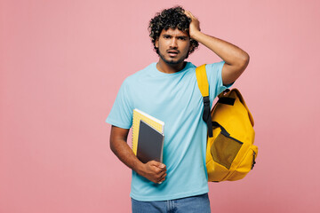 Young puzzled sad confused smart Indian boy student wear blue t-shirt casual clothes backpack bag hold books put hand on head isolated on plain pink background. High school university college concept.
