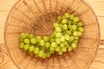 Bunch of ripe seedless grapes in a straw dish on a wooden table, macro, top view.