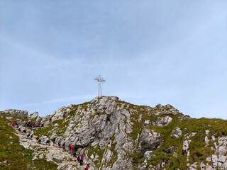 Fototapeta premium Hikers making their way up a mountain trail towards a large metal cross on a sunny day