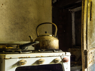 Rustic kitchen with an old kettle on a vintage stove in an abandoned home during daytime