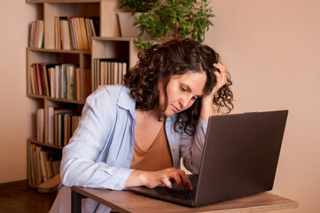 Sad woman using laptop sitting at table in wrong position and propping her face with her hand.