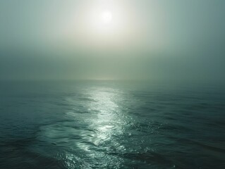 Calm ocean waters reflecting dulled sunlight under a thick layer of fog in the early morning hours