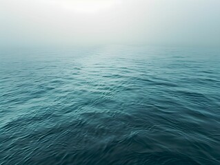 Obraz premium Calm ocean waves gently lap in a tranquil, foggy atmosphere during early morning light near a serene coastline