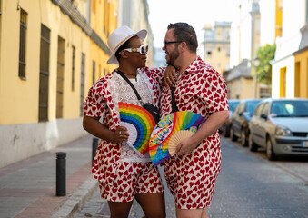 Naklejka premium Gay couple with a hand fan with the colors of the LGTBI flag