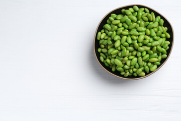 Fresh edamame soybeans in bowl on white wooden table, top view. Space for text