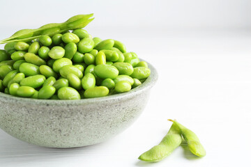 Fresh edamame soybeans in bowl and pods on white wooden table, closeup