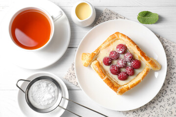 Tasty puff pastry with raspberries and tea on white wooden table, flat lay