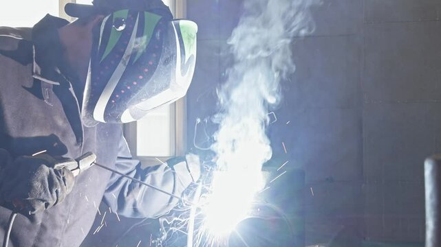 An industrial worker welds a large metal pipe within a workshop, outfitted in protective gear and surrounded by various mechanical tools, showcasing the precision and skill of metalworking professiona