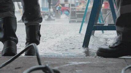 A worker wearing protective boots stands beside industrial pipeline equipment in a heavy rain, emphasizing the importance of safety gear and the resilience required in harsh weather conditions.