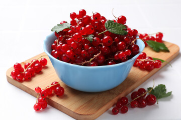 Fresh red currants in bowl and green leaves on white table, closeup
