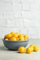 Ripe plums in bowl on light textured table
