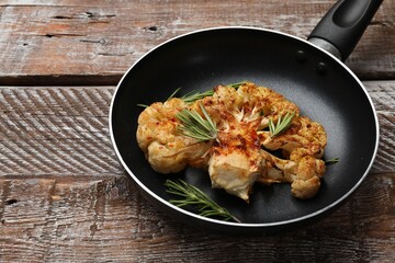 Tasty cauliflower steak and rosemary in frying pan on wooden table, closeup