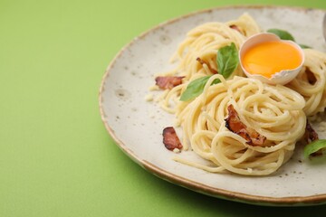 Delicious pasta Carbonara served on green background, closeup