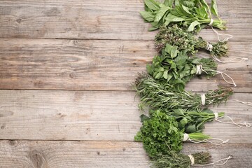 Bunches of different aromatic herbs on wooden table, flat lay. Space for text