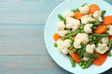 Tasty cooked cauliflower with green peas, string beans and carrot slices on light blue wooden table, top view. Space for text