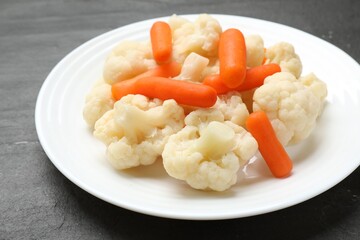 Tasty cauliflower with baby carrots on black table, closeup