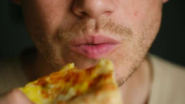 Bearded man bites off slice of cheesy pizza resting at home. Guy chews enjoying delicious taste of unhealthy snack with crispy edges for dinner
