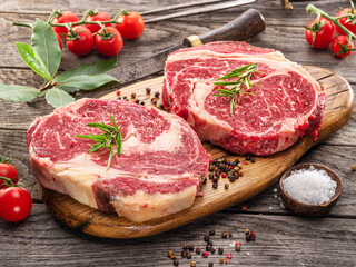 Fototapeta premium Raw beef steaks with herbs and spices ready for cooking are on wooden board.