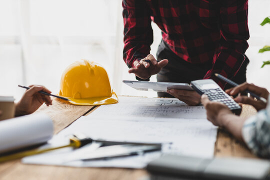 Brainstorming group of architects and engineers discuss building blueprint design paperwork and drawing construction project planning on wooden table in office. Construction project budget planning.