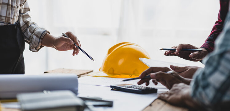 Brainstorming group of architects and engineers discuss building blueprint design paperwork and drawing construction project planning on wooden table in office. Construction project budget planning.
